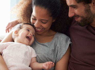 A diverse family snuggling with their newborn child.