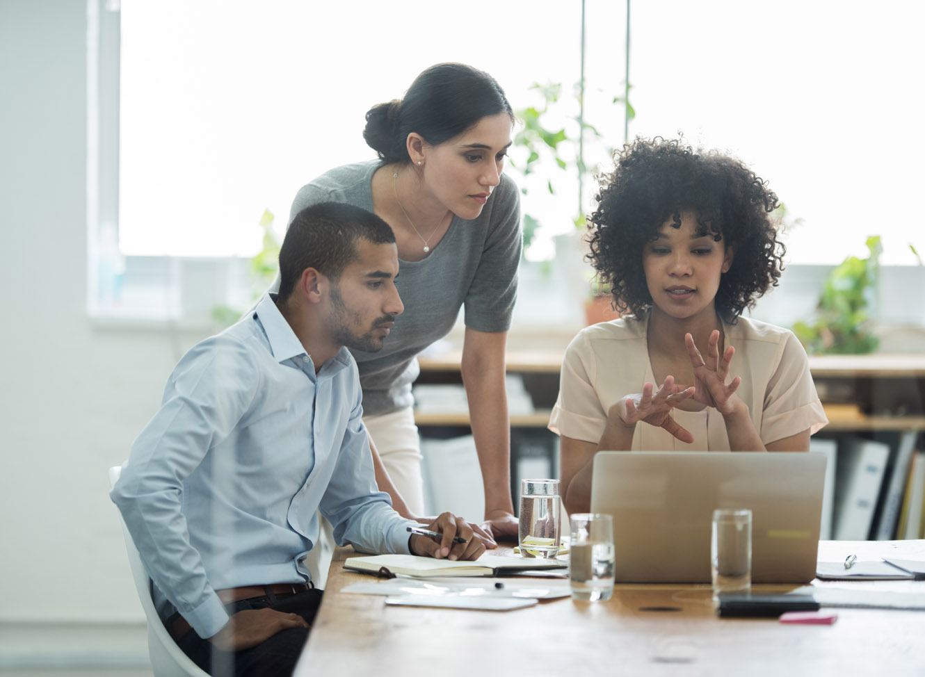 Two women and a man in an office look at a laptop together.