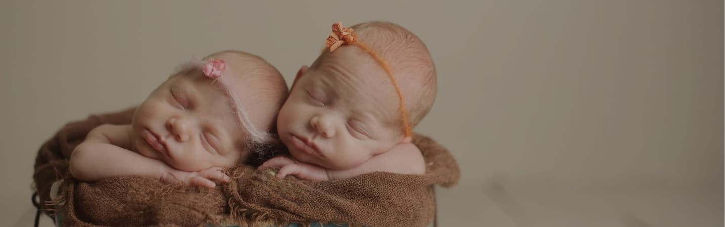 newborn twin girls sleeping in a basket