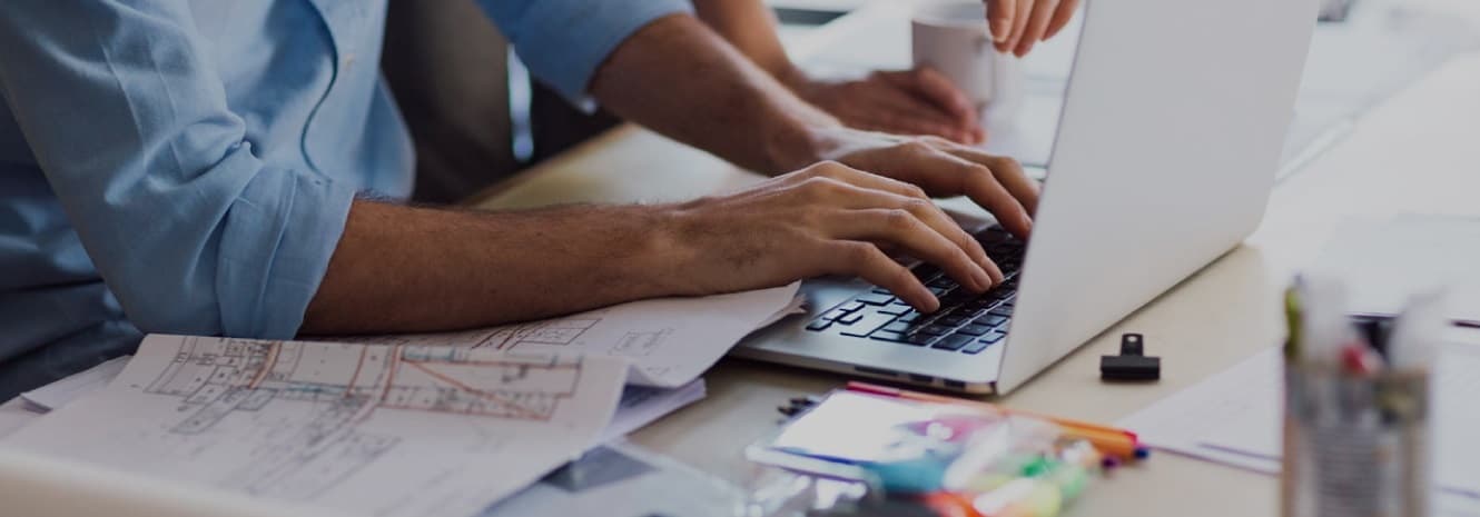 man's hands working on laptop with blueprints