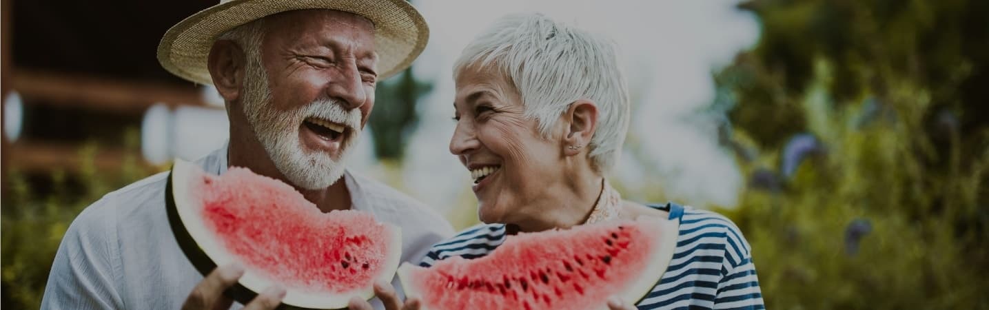 Cheerful mature couple having fun while eating watermelon outside