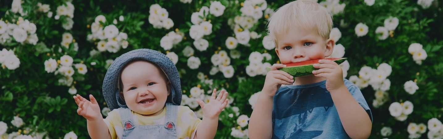 Brother and sister toddlers eating watermelon in the park