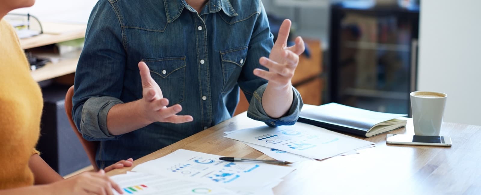 Businessman speaking with hands sitting at desk with co-worker