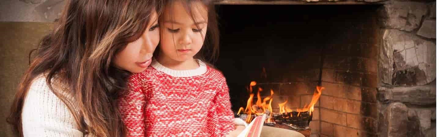 Asian mother reading to her daughter by the fireplace
