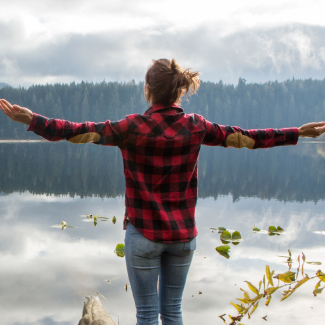 Woman facing a lake with arms out wide.