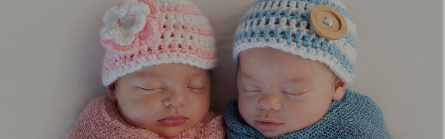 Newborn twins in knit caps swaddled in blankets