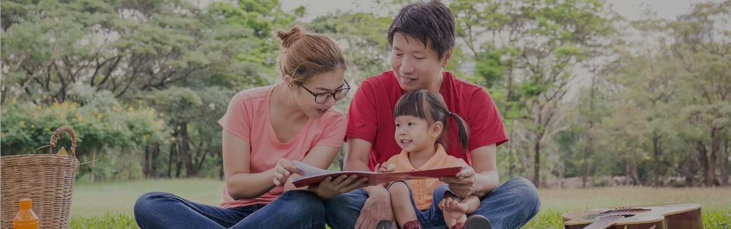 Happy asian parents reading a book with toddler daughter