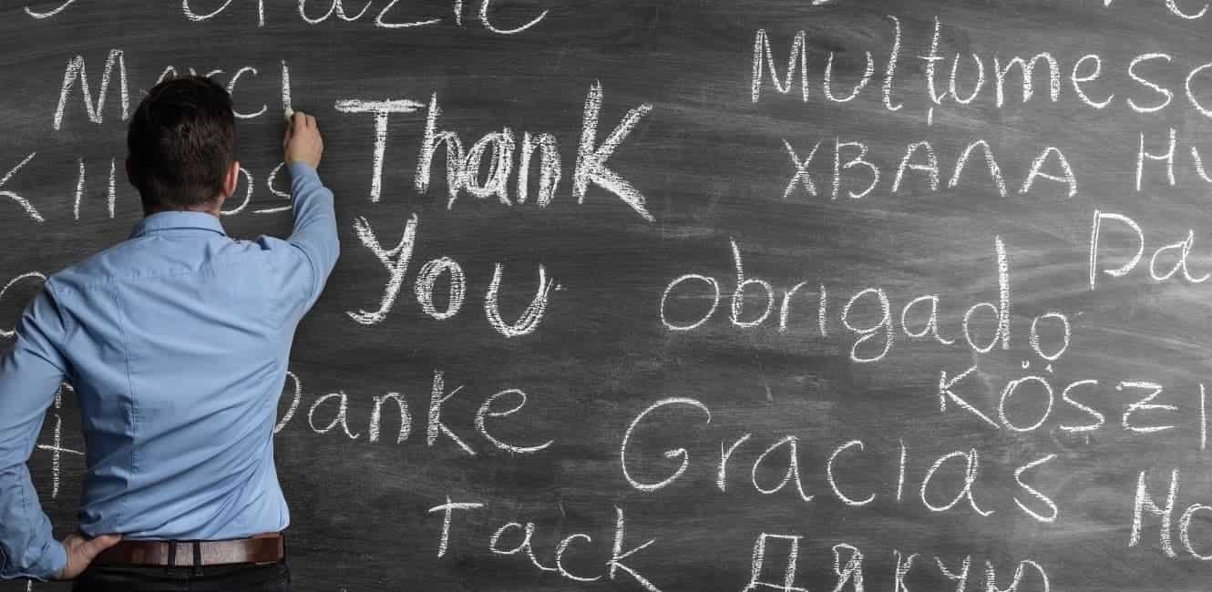 Man writing thank you in many languages on blackboard.