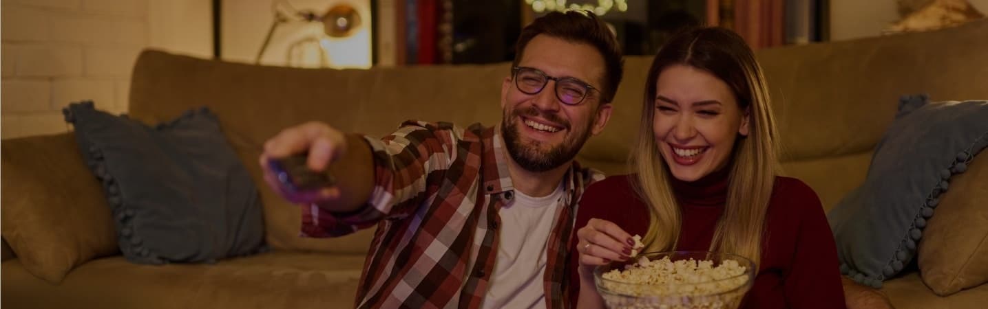 Happy young couple watching TV and eating popcorn.
