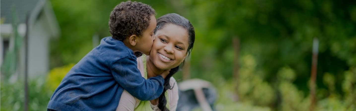 mom carrying son on back as he kisses her cheek